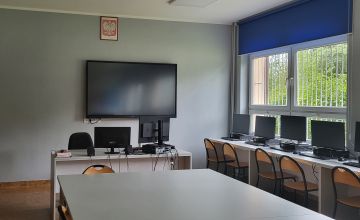 Odnowiona sala lekcyjna. Z prawej strony okno przysłonięte nebieską roletą. Pod białymi ścianami stoją jasne biurka z komputerami.
